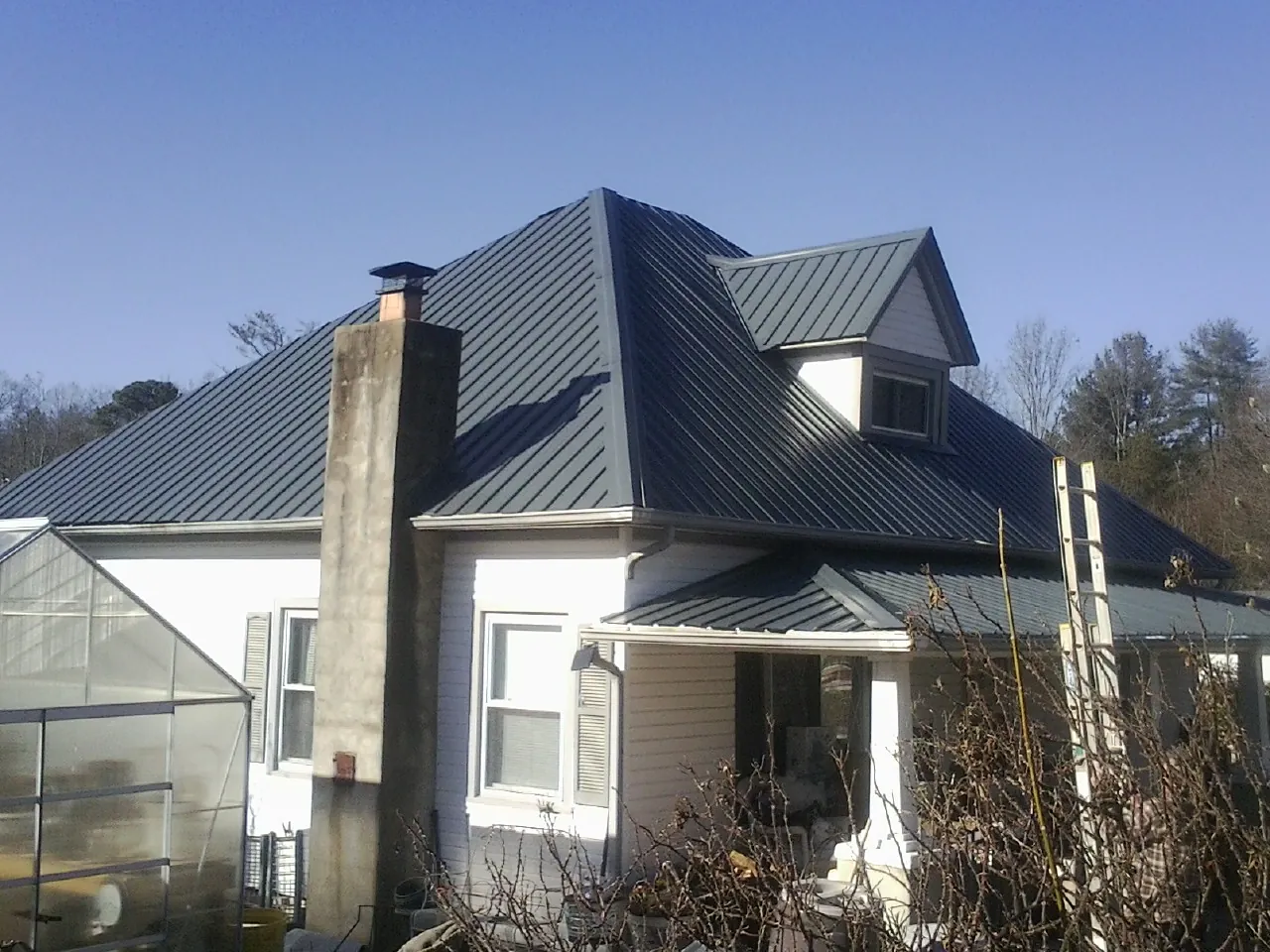 Dark blue standing seam metal roof on a white farmhouse with dormer — Slate & Tile Roof Repair by Roofing Brothers in East Berne