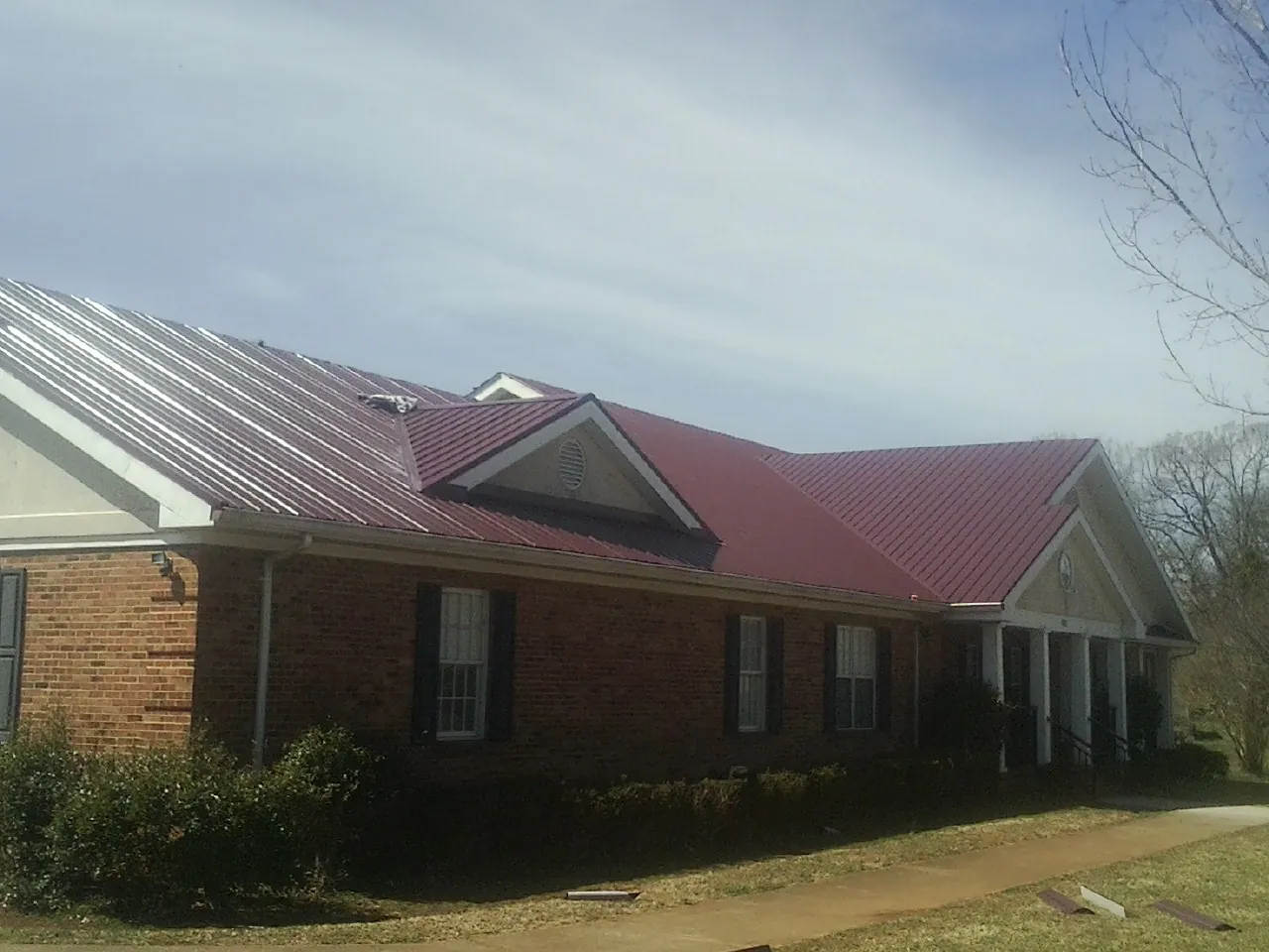 Red metal roof with gabled entries on a long brick building, from a Hail Damage Roof Repair job in East Berne