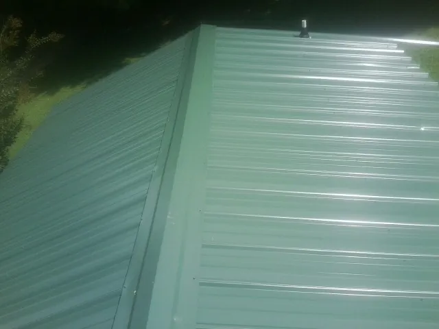 New green metal panels meeting at the ridge of a roof — Flat Roof Repair work by our crew in East Berne