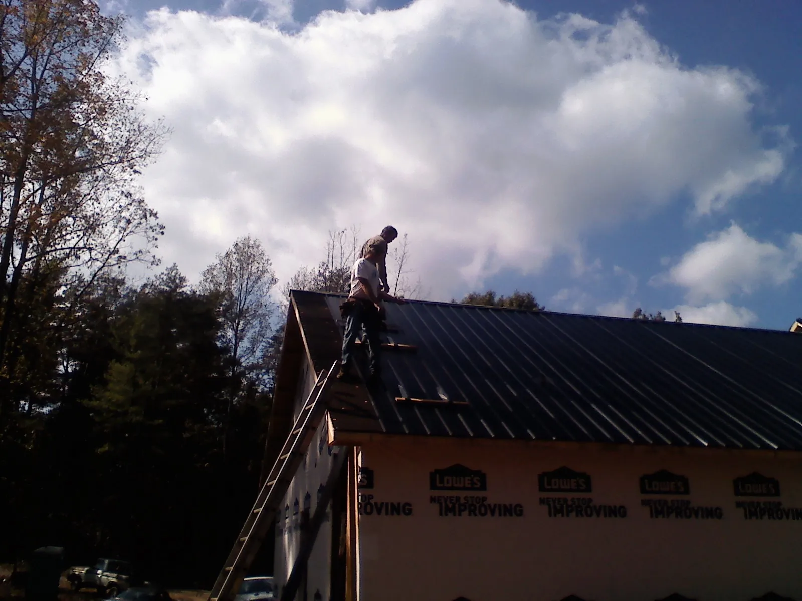 Roofer fastening dark metal panels high against a cloudy sky, from a Roof Inspection job in East Berne