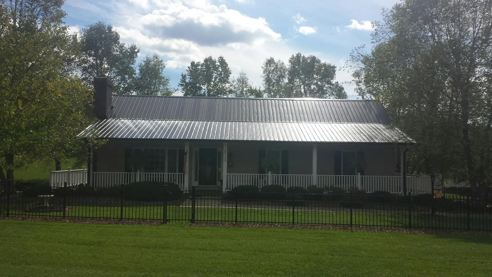 Gray metal roof on a brick ranch with a full width front porch — Gutter Guard Installation work by our crew in East Berne
