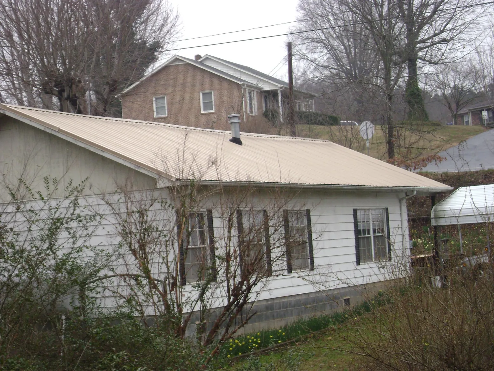 Tan metal roof on a white sided house set into a hillside — Commercial Roofing by Roofing Brothers in East Berne